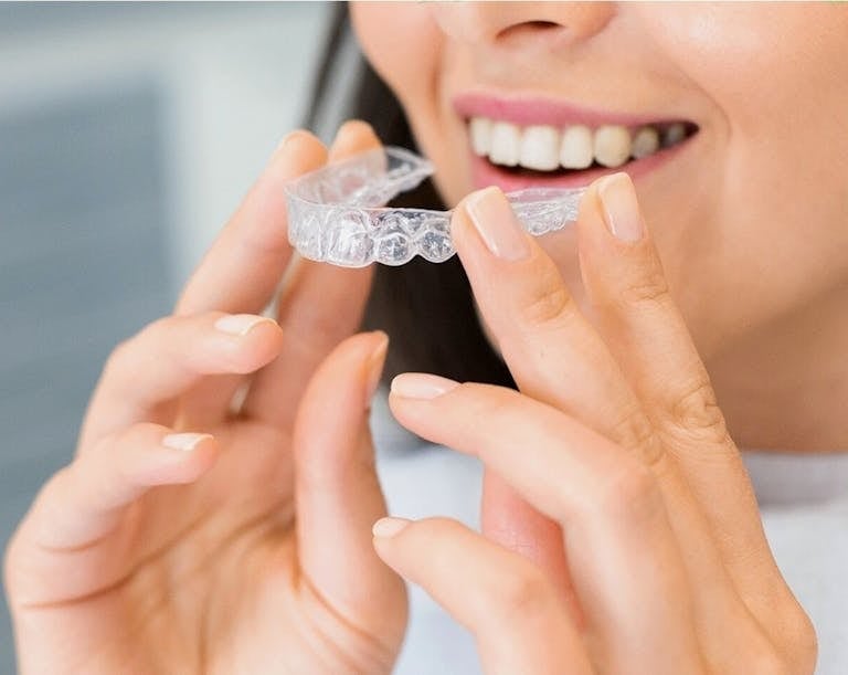 smiling woman holding clear aligners like invisalign